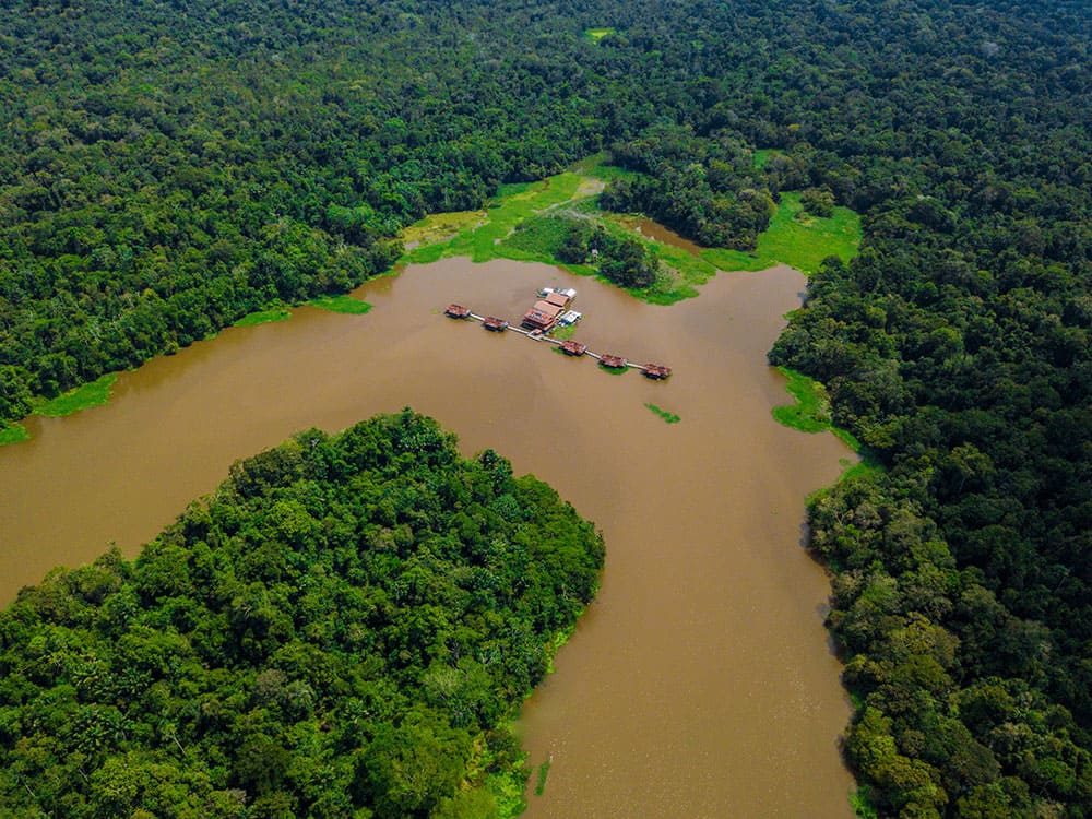 Luchtfoto van een ecolodge met drijvende structuren op een kronkelende rivier, volledig omringd door dicht bos. Luchtfoto van een ecolodge met drijvende structuren op een kronkelende rivier, volledig omringd door dicht bos.