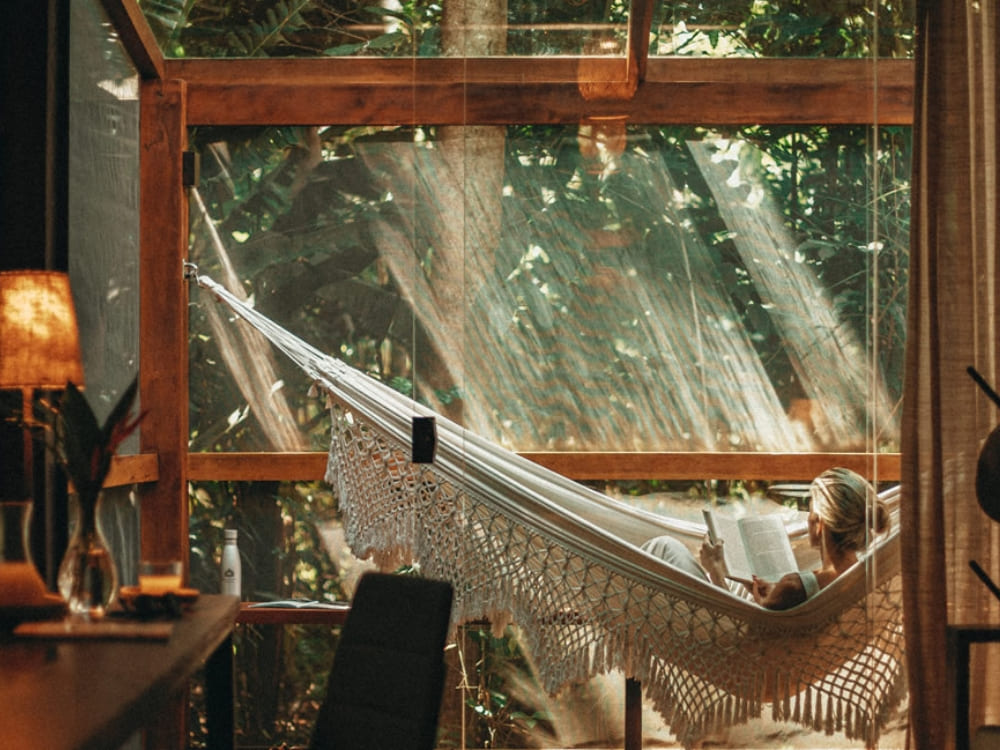 Een persoon ontspant in een hangmat in een verfijnde kamer met grote glazen ramen die uitkijken op de jungle. Een persoon ontspant in een hangmat in een verfijnde kamer met grote glazen ramen die uitkijken op de jungle.