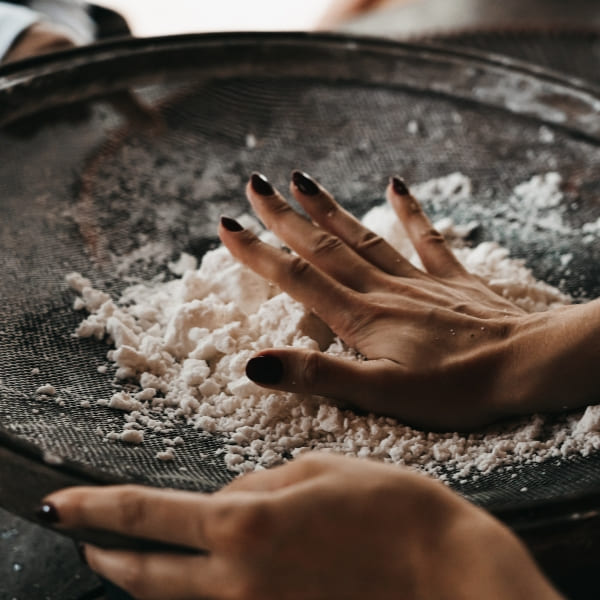 A person sifting a white substance through a round sieve during a cultural tour of riverside communities.